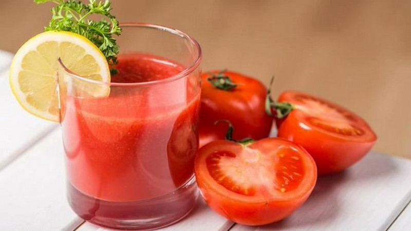 a-glass-filled-with-red-liquid-sitting-next-to-two-tomatoes-on-a-plate