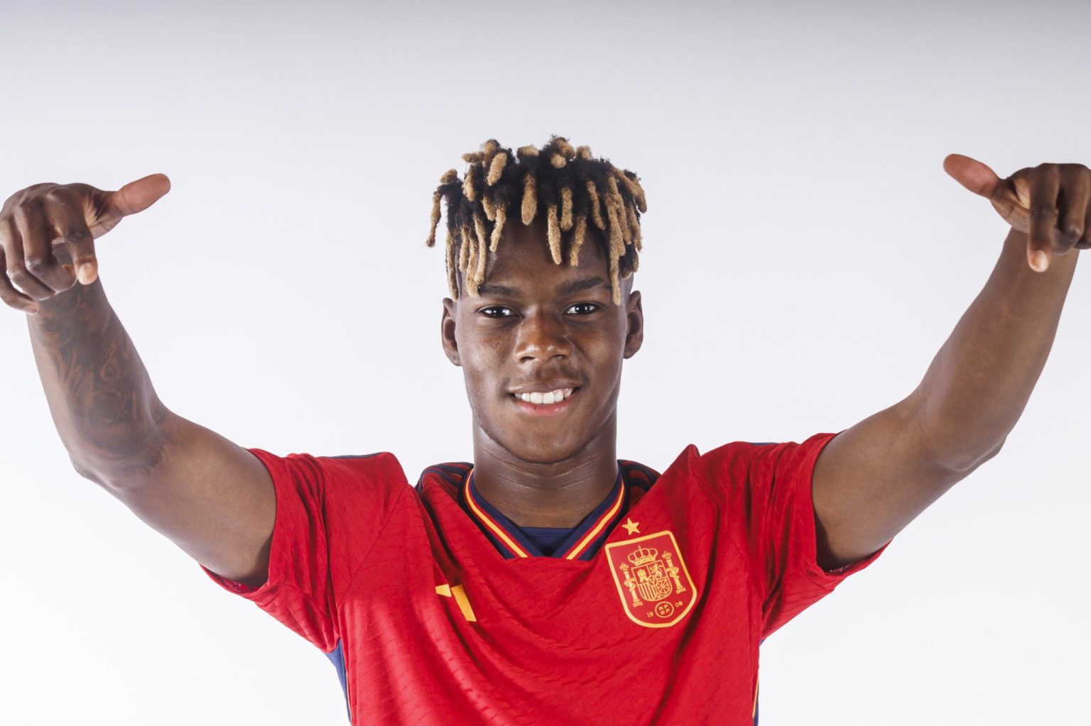  Nico Williams, a Spanish professional soccer player, is all smiles while posing in his red jersey with his arms in the air.